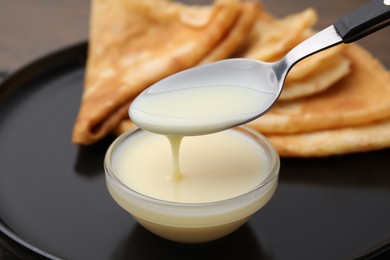 Photo of Taking tasty condensed milk from bowl with spoon at table, closeup