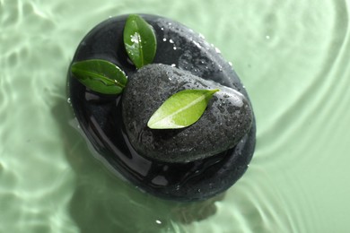 Photo of Spa stones and fresh leaves in water on light green background, top view