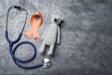 Orange ribbon, toy bear and stethoscope on grey table, flat lay with space for text. Multiple sclerosis awareness