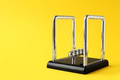 Newton's cradle on yellow background, space for text. Physics law of energy conservation