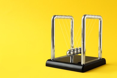 Photo of Newton's cradle on yellow background, space for text. Physics law of energy conservation