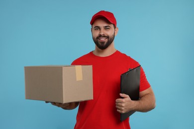 Happy young courier with parcel and clipboard on light blue background