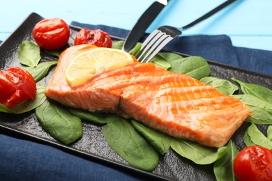 Tasty grilled salmon with tomatoes, spinach and lemon served on table, closeup