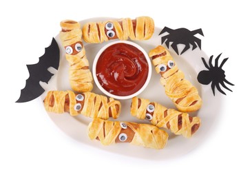 Photo of Plate with tasty sausage mummies, Halloween decorations and ketchup isolated on white, top view