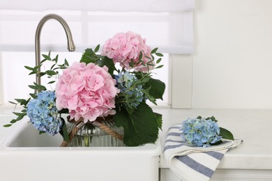 Photo of Vase with beautiful hortensia flowers in kitchen sink