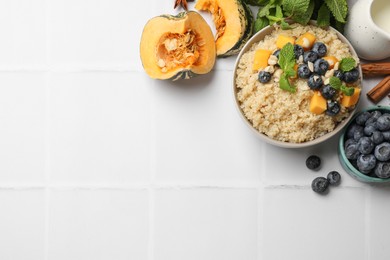 Photo of Flat lay composition with bowl of tasty quinoa porridge, blueberries and pumpkin on white tiled table. Space for text