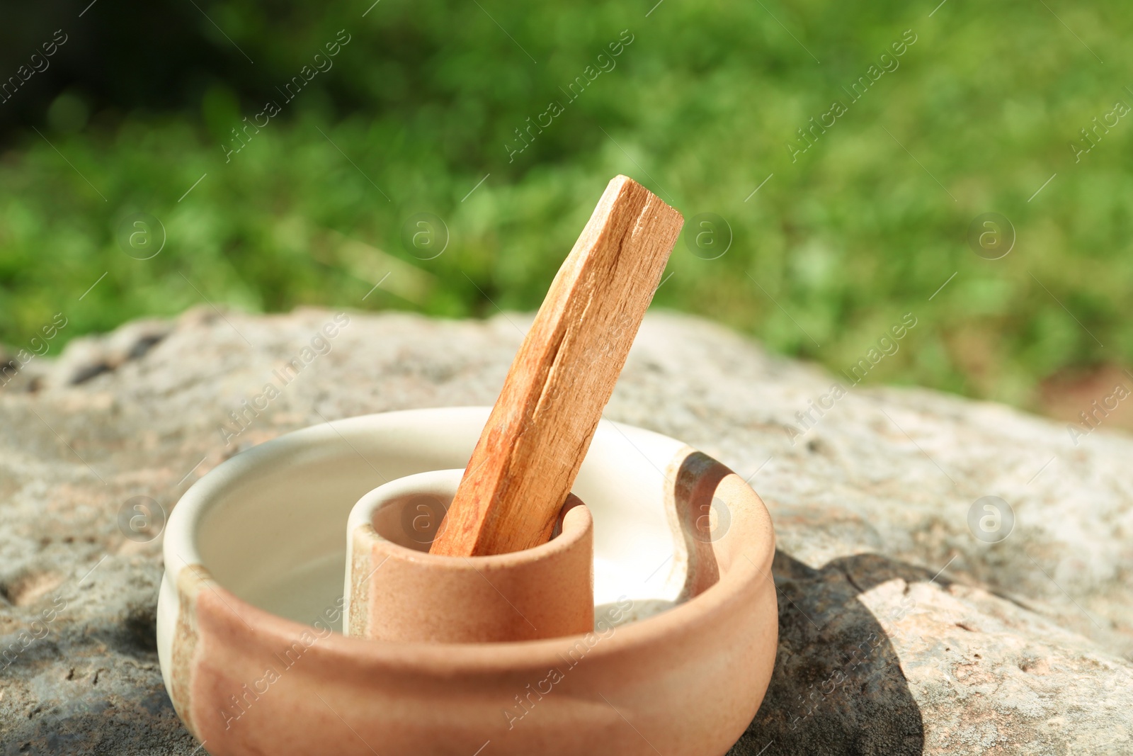 Photo of Palo santo stick in holder on stone outdoors, closeup