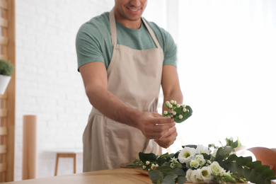 Florist making beautiful bouquet at table in workshop, closeup