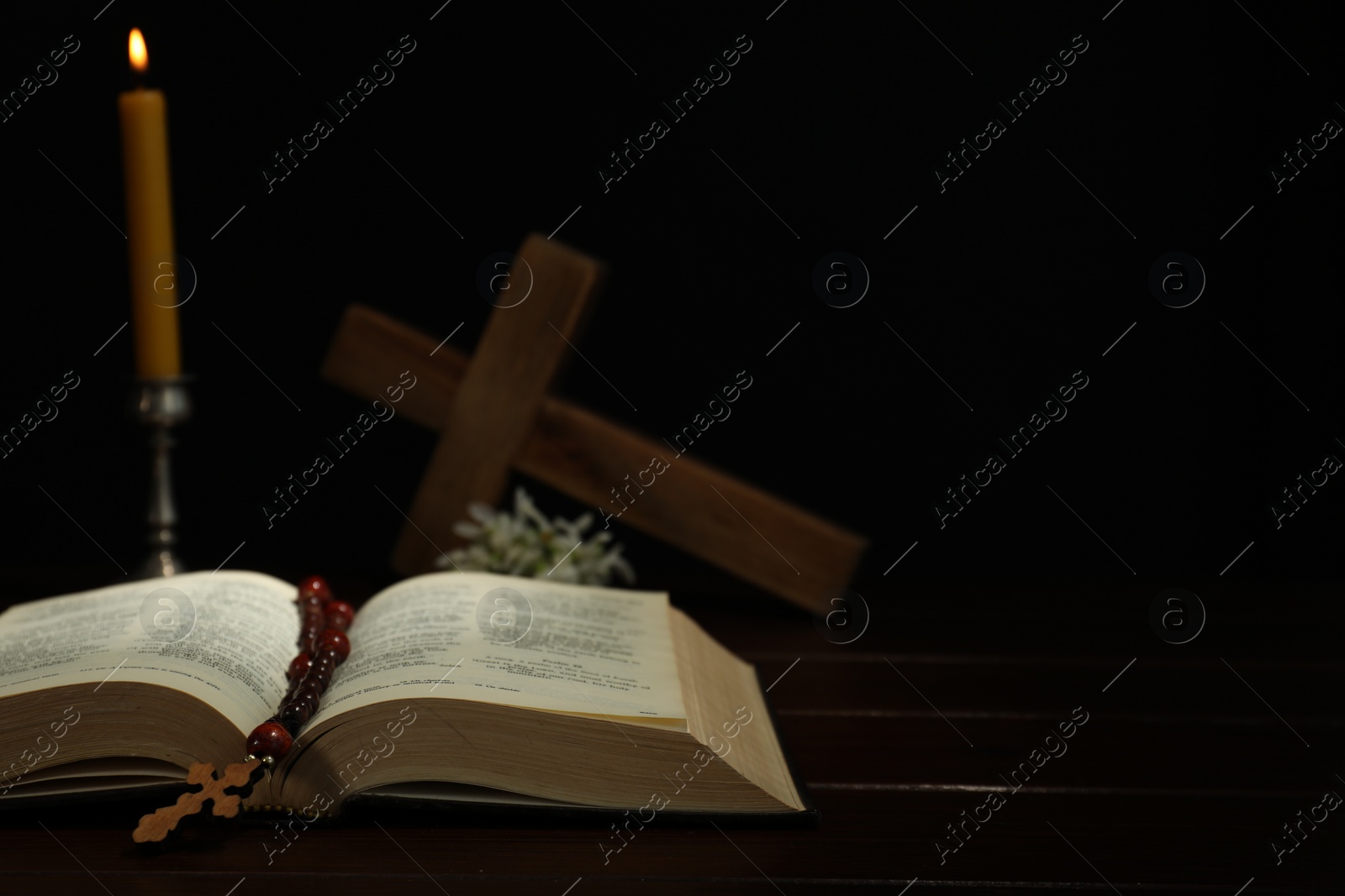 Photo of Crosses, rosary beads, Bible and church candle on wooden table, space for text
