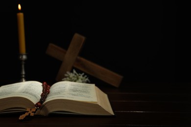 Photo of Crosses, rosary beads, Bible and church candle on wooden table, space for text