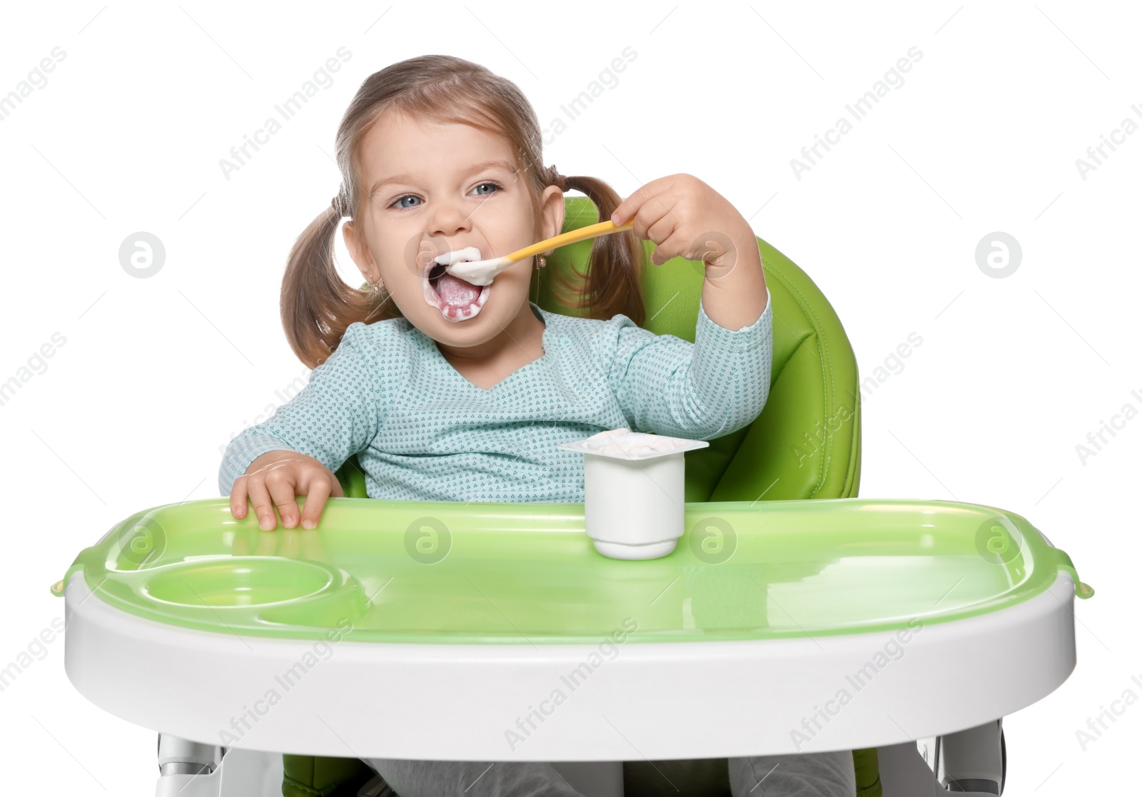 Photo of Cute little child eating tasty yogurt from plastic cup with spoon in high chair on white background