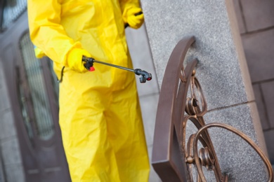 Photo of Person in hazmat suit disinfecting railing with sprayer outdoors, closeup. Surface treatment during coronavirus pandemic
