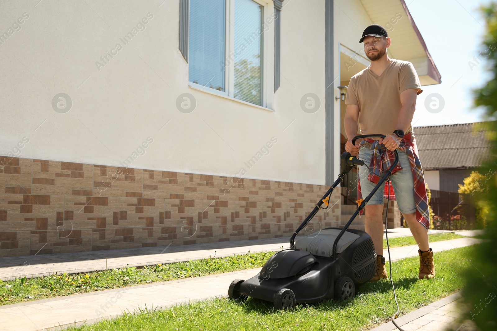 Photo of Man cutting green grass with lawn mower on backyard