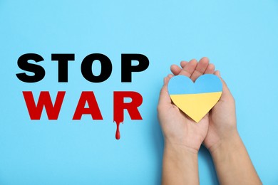 Image of Stop War in Ukraine. Woman holding paper heart in colors of Ukrainian flag on light blue background, closeup