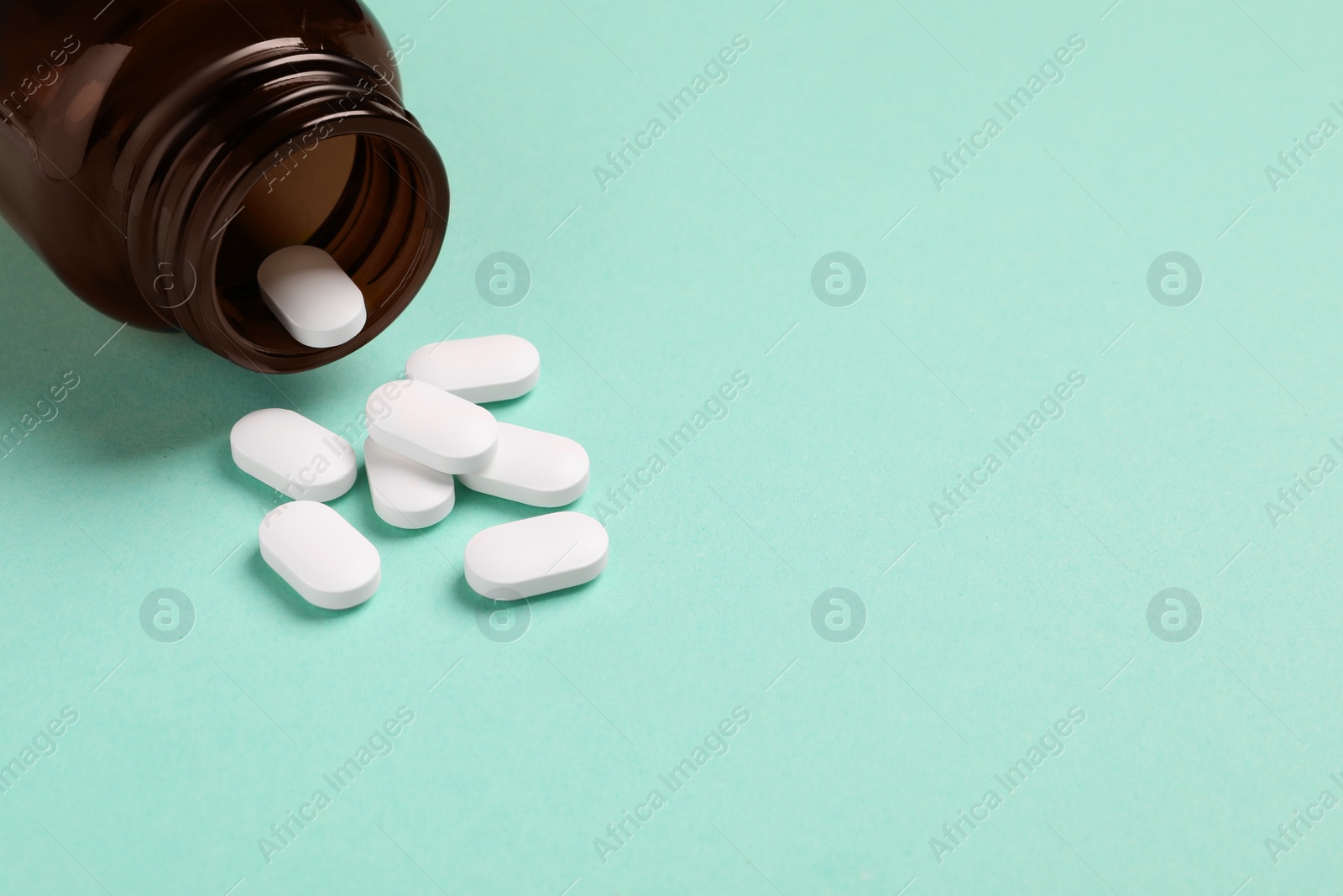 Photo of Plastic medical bottle with pills on turquoise background, closeup. Space for text