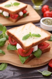 Photo of Delicious Caprese sandwich with mozzarella, tomatoes, basil and pesto sauce on wooden table, closeup