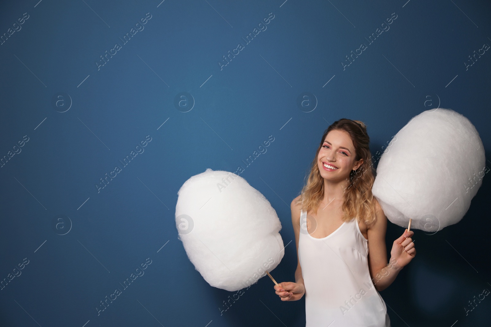 Photo of Portrait of pretty young woman with cotton candy on blue background. Space for text