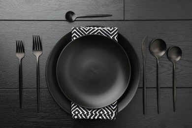 Stylish setting with cutlery and plates on black wooden table, flat lay