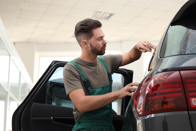 Worker tinting car window with foil in workshop