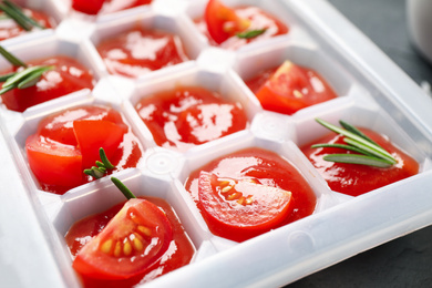Photo of Ice cube tray with tomatoes, sauce and fresh rosemary, closeup