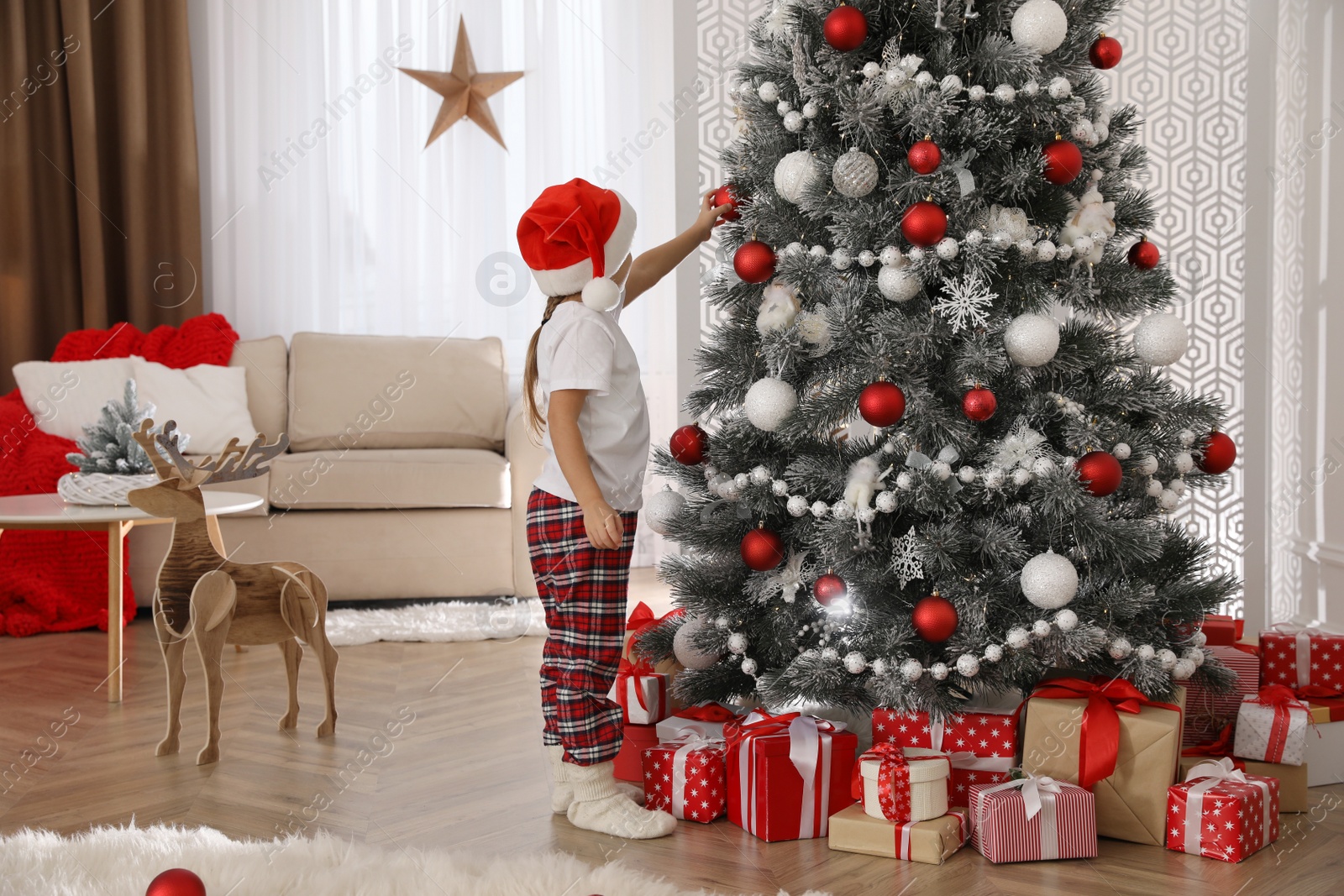 Photo of Cute little girl decorating Christmas tree at home