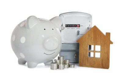 Electricity meter, house model, piggy bank and stacked coins on white background