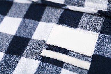 Photo of Blank clothing label on checkered shirt, closeup. Space for text