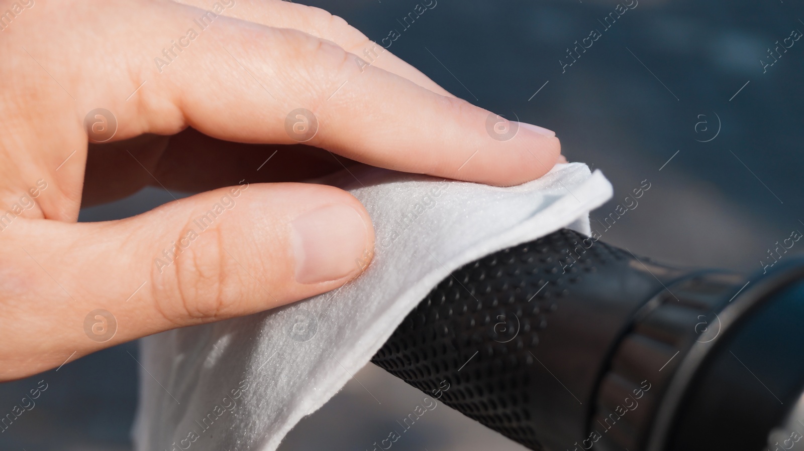 Photo of Man cleaning scooter steering wheel with wet wipe outdoors, closeup. Protective measures