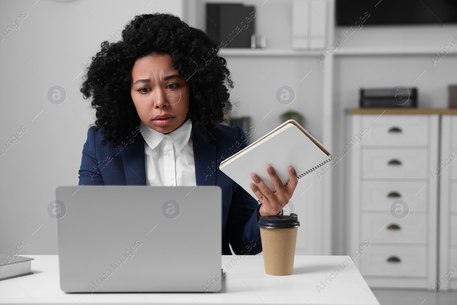 Photo of Deadline concept. Tired woman looking at laptop and holding notepad in office