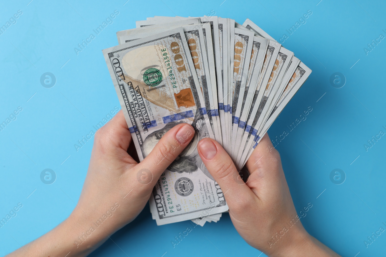 Photo of Money exchange. Woman holding dollar banknotes on light blue background, top view