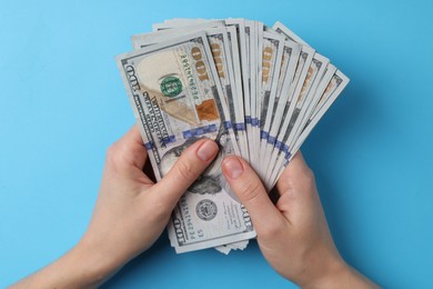 Money exchange. Woman holding dollar banknotes on light blue background, top view