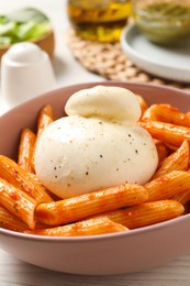 Photo of Bowl of delicious pasta with burrata and tomato sauce on white wooden table, closeup