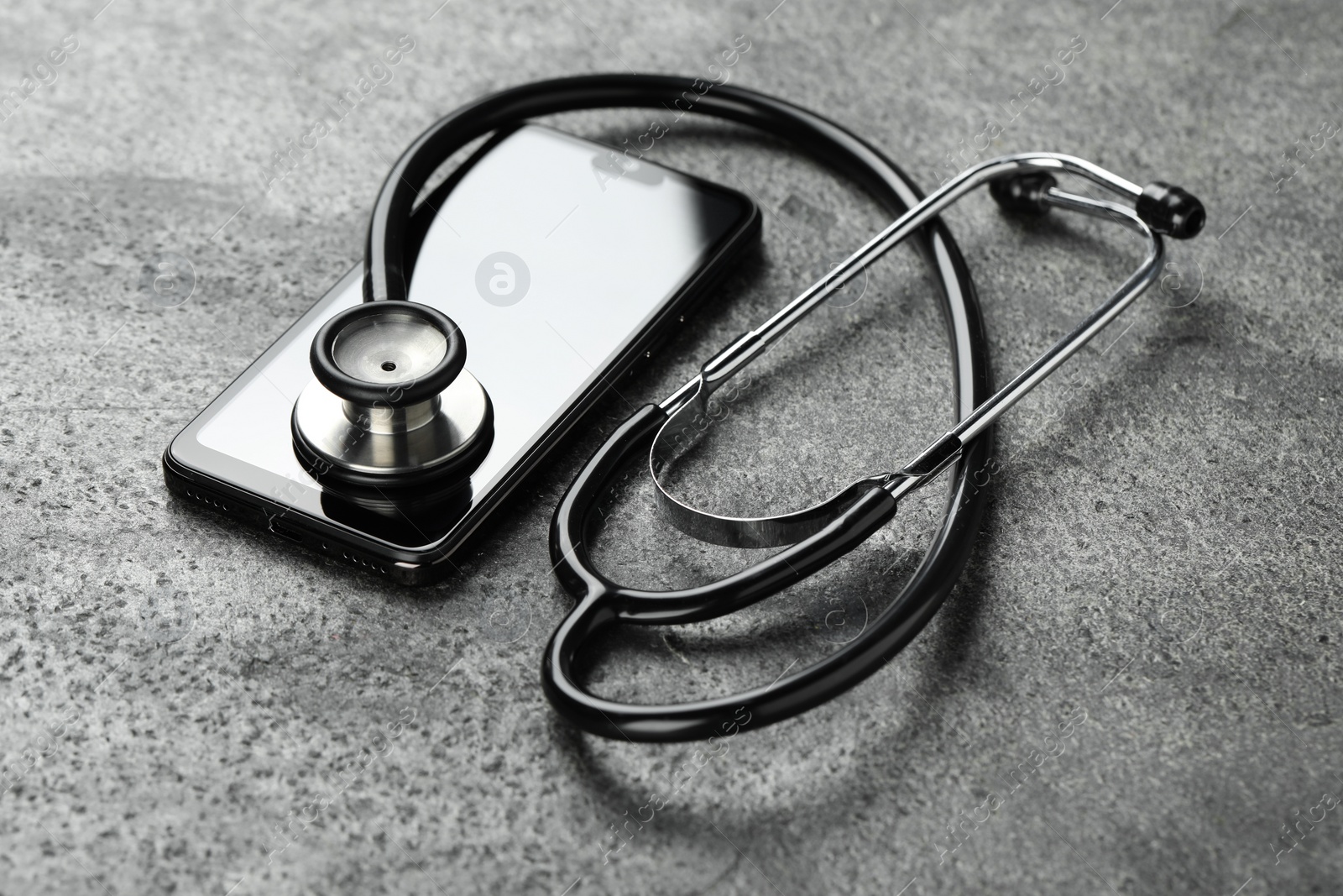 Photo of Modern smartphone and stethoscope on grey table