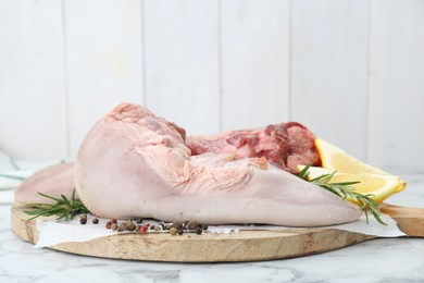 Photo of Raw beef tongues, peppercorns, salt, rosemary and lemon on white marble table, closeup