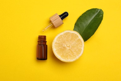 Photo of Bottle of citrus essential oil, pipette and fresh lemon on yellow background, flat lay
