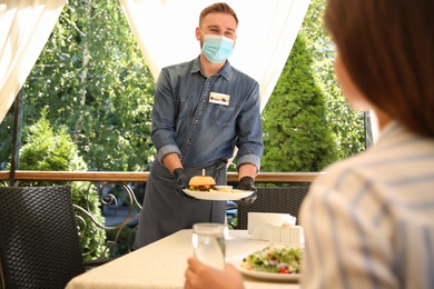 Photo of Waiter serving food to customer in restaurant. Catering during coronavirus quarantine