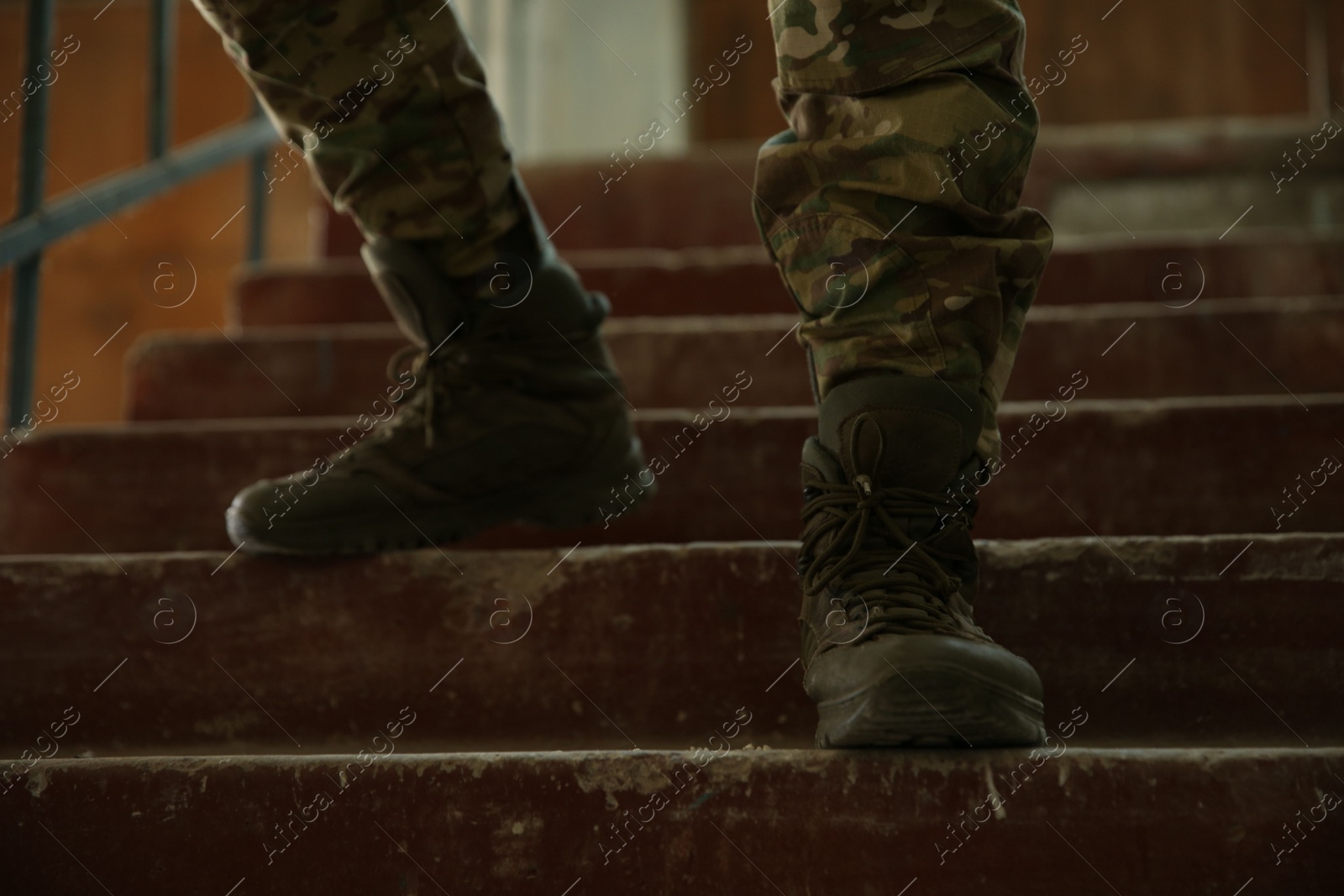 Photo of Military mission. Soldier in uniform on stairs inside abandoned building, closeup