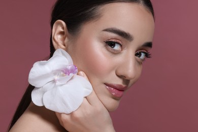 Photo of Portrait of beautiful young woman with orchid flower on dark pink background, closeup