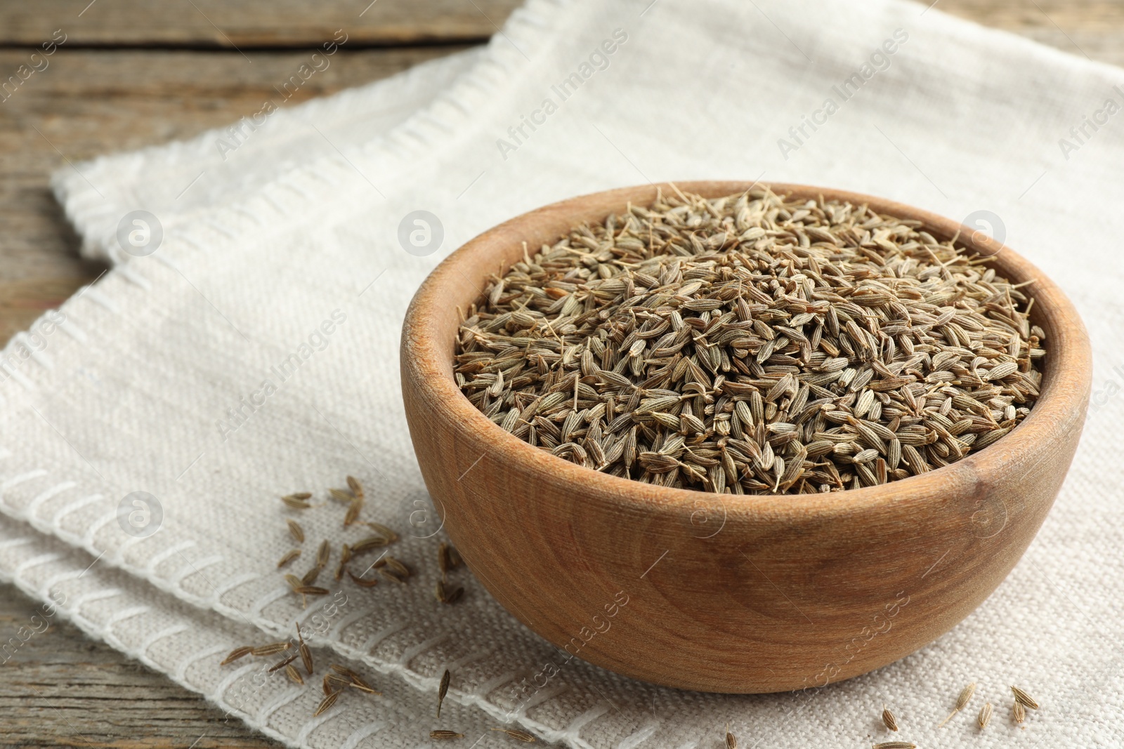 Photo of Bowl of caraway seeds and napkin on wooden table, closeup. Space for text