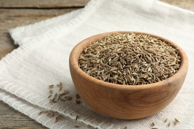 Bowl of caraway seeds and napkin on wooden table, closeup. Space for text