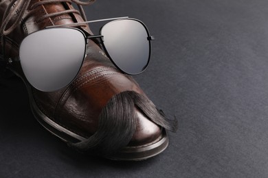 Photo of Artificial moustache, shoe and sunglasses on black background, closeup. Space for text