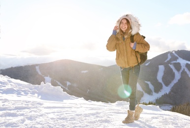 Happy young woman with backpack spending winter vacation in mountains. Space for text