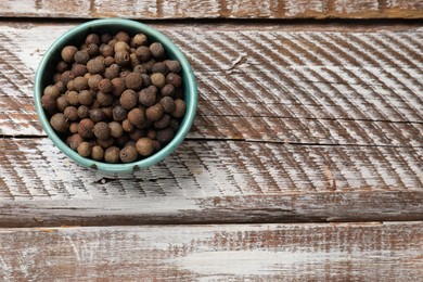 Photo of Aromatic allspice pepper grains in bowl on wooden table, top view. Space for text