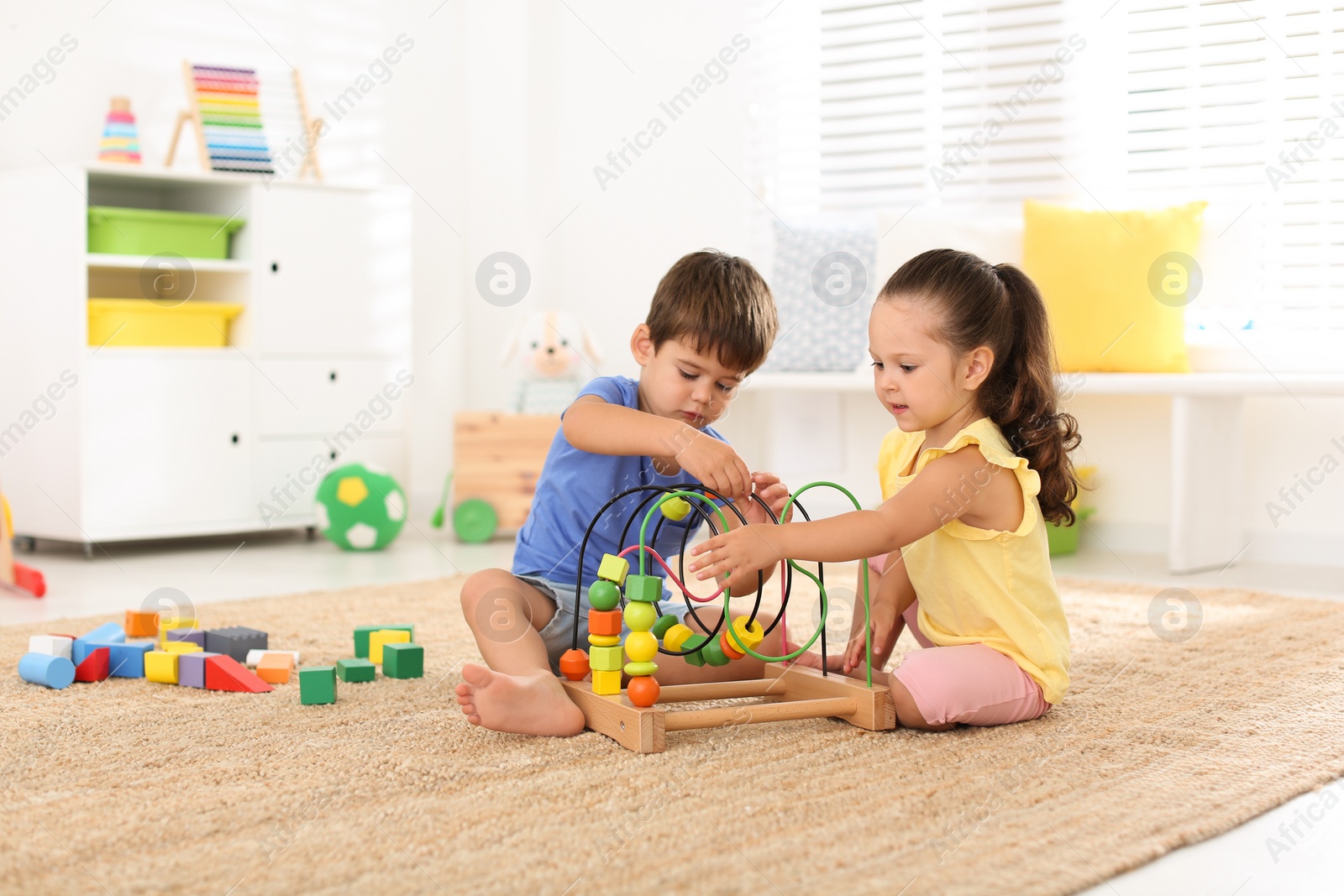 Photo of Cute little children playing with bead maze on floor at home. Educational toy