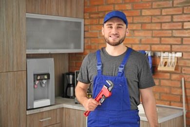 Professional plumber in uniform with pipe wrench indoors