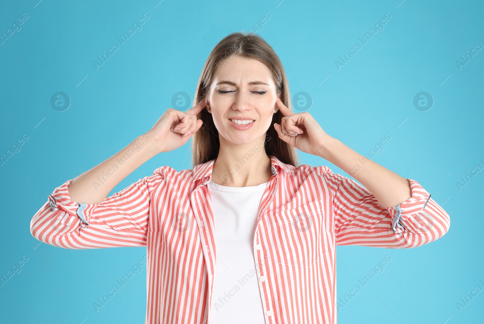 Photo of Emotional young woman covering her ears with fingers on light blue background