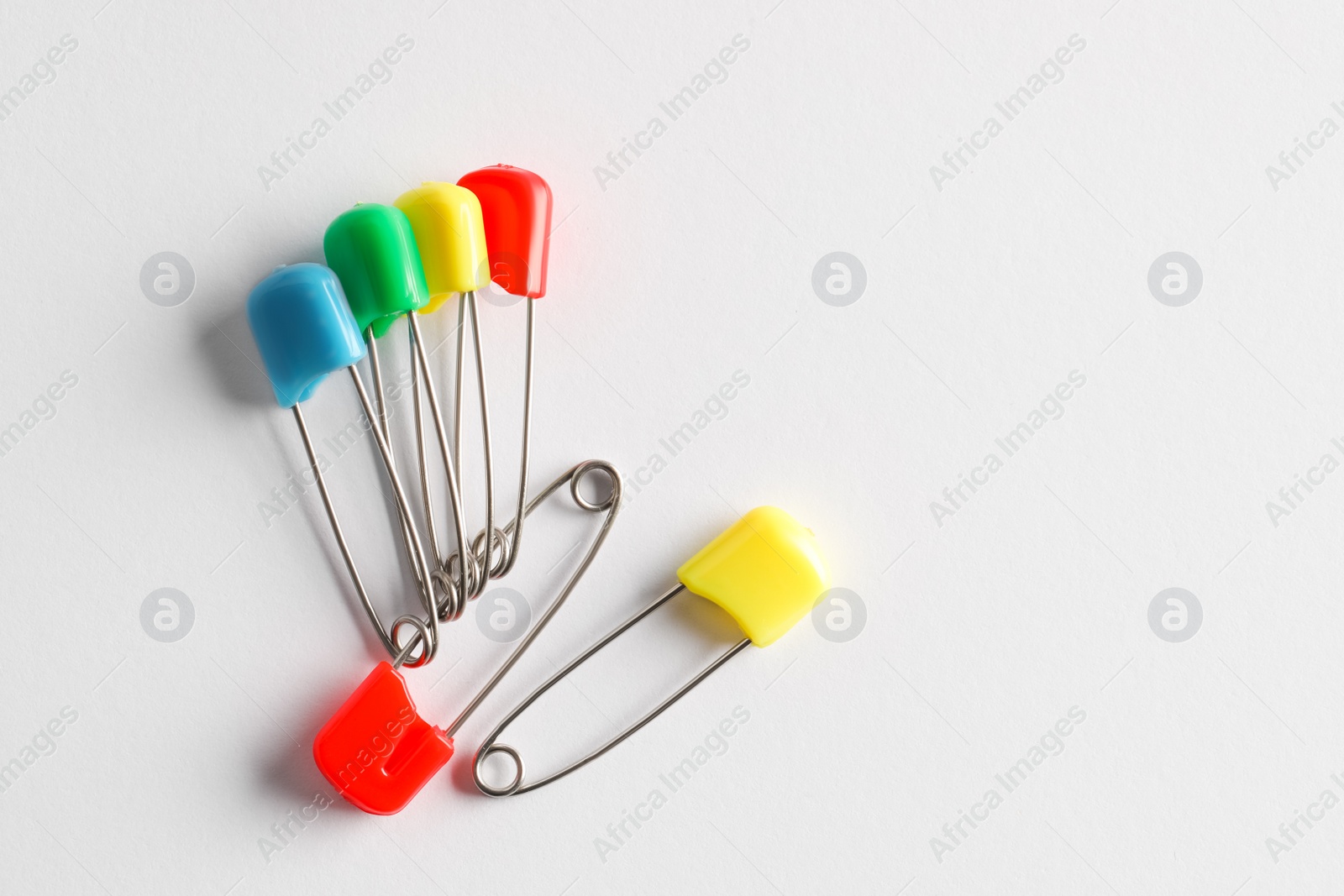 Photo of Colorful safety pins on white background, flat lay. Space for text