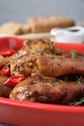 Chicken legs glazed in soy sauce with black sesame, chili pepper and thyme in red bowl, closeup