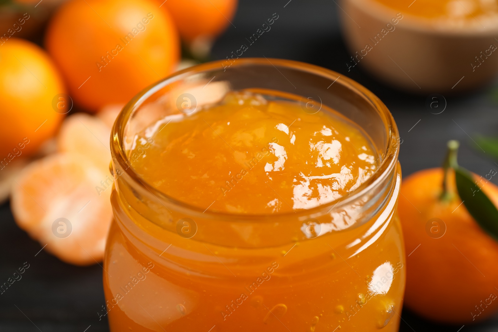 Photo of Tasty tangerine jam in glass jar on table, closeup