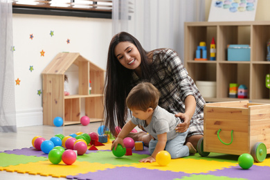 Young nanny and cute little baby playing with toys at home